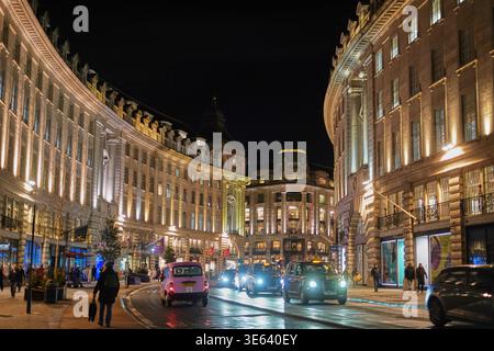 Vista notturna di una strada curva fiancheggiata da grandi edifici storici illuminati da luci calde a Londra, Regno Unito. L'asfalto bagnato riflette l'edificio Foto Stock
