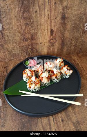 Colpo ad angolo alto di deliziosi sushi panini al forno con salmone, formaggio fuso e salsa mayo piccante. Servito con bacchette di legno, zenzero sottaceto, Foto Stock