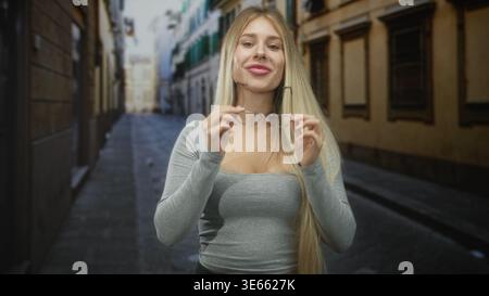 Donna che tiene gli occhiali da vista e sorride su una stretta strada acciottolata tra vecchi edifici, capelli lunghi visibili e scollatura; sicurezza. Foto Stock