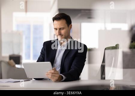 Uomo d'affari ispanico adulto che esamina documenti utilizzando un tablet in ufficio Foto Stock
