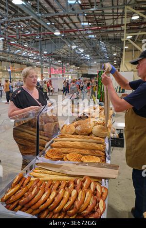 Una donna che compra pane fresco fatto in casa da un venditore, una stalla, un commerciante. Presso l'Old Bus Depot Markets di Canberra, Australia. Foto Stock