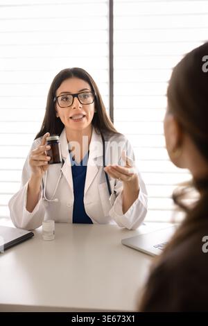 Medico che tiene in mano una bottiglia di pillole, che spiega i farmaci prescritti al paziente Foto Stock