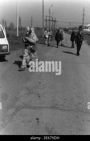 Mykolaivka, 1998 anni, stabilimento AIZ per la difesa civile. Un operaio specializzato che indossa una tuta di protezione chimica completa e una maschera antigas conduce la ricognizione tattica su una strada in cemento. Il civile dedicato gestisce un dosimetro specializzato per radiazioni con una sonda durante un esercizio di risposta realistico di emergenza, mentre i giudici osservano in background. Questa straordinaria immagine d'archivio illustra l'addestramento attivo per la sopravvivenza alle catastrofi, i protocolli di sicurezza industriale e le routine essenziali di pubblica sicurezza nel pacifico Donbas. Foto Stock