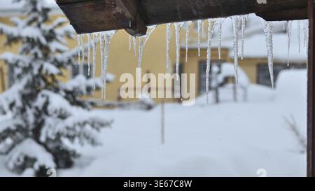 Ghiaccioli appesi da un tetto di legno in un paesaggio invernale innevato all'aperto Foto Stock