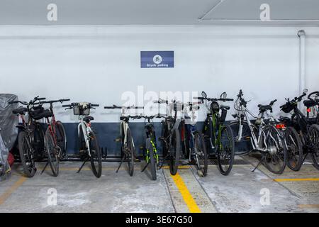 Molte biciclette diverse si trovano lungo un muro di cemento bianco in un moderno parcheggio sotterraneo di un lussuoso complesso residenziale Foto Stock