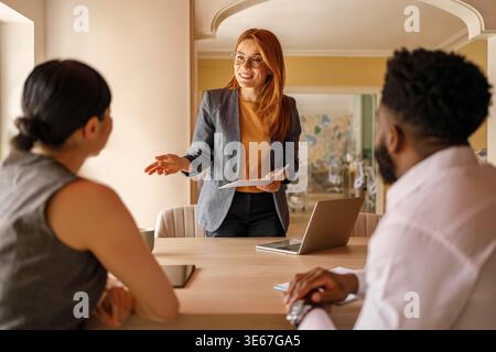 Manager donna che esamina il documento mentre discute le idee con i colleghi mentre è in piedi alla scrivania durante la riunione d'ufficio Foto Stock