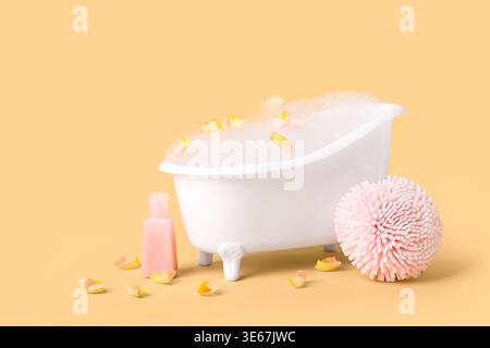 Piccola vasca da bagno con schiuma, petali di fiori, spugna e bottiglia di prodotto cosmetico su sfondo colorato Foto Stock