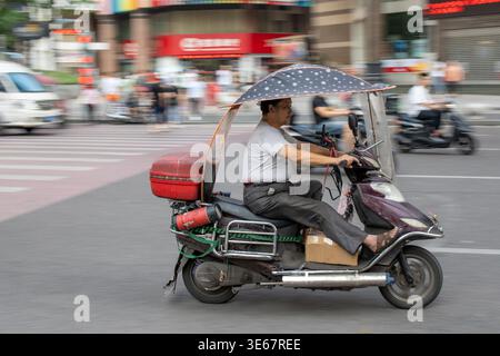 Chongqing, Cina - Agosto 2019 : uomo che guida pericolosamente veloce in uno scooter sulla strada congestionata Foto Stock