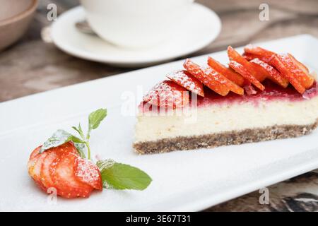 Un pezzo di deliziosa cheesecake con frutti di bosco su un vero tavolo da caffè da vicino. Tazza di caffè sullo sfondo Foto Stock