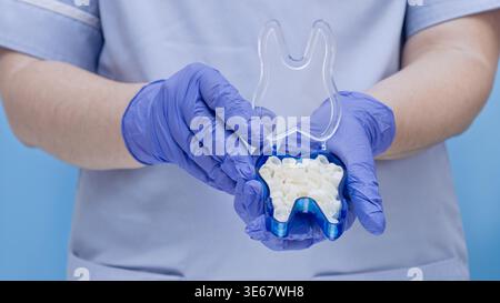 Il medico sta tenendo in mano una scatola di plastica blu aperta a forma di dente, piena di corone dentarie temporanee bianche. Restauro dentale, protesi e o Foto Stock