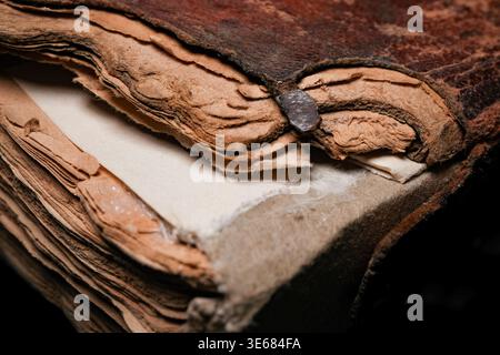 Primo piano del dorso di un libro antico e usurato e delle pagine con carta lacerata e ingiallita e una chiusura in metallo arrugginito, copertina in pelle testurizzata e bordi sfilacciati Foto Stock