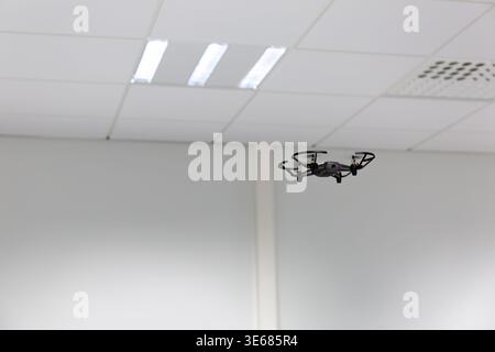 Piccolo drone in volo in una stanza bianca vuota. Un piccolo drone quadricottero è a metà volo in una stanza bianca. Foto Stock