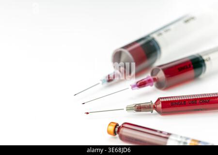 Diverse siringhe mediche monouso riempite di sangue con aghi ipodermici appuntiti esposti e goccioline rosse visibili sistemate con cura Foto Stock