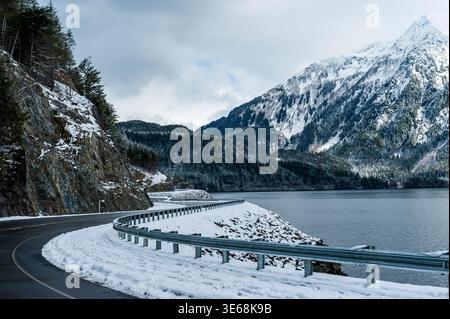 La tortuosa Sawmill Creek Road si snoda lungo Silver Bay in un paesaggio invernale. La neve copre il terreno, le scogliere e le maestose montagne di Sitka, Alaska. Foto Stock