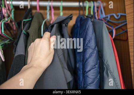 Giacca invernale a mano su appendiabiti nell'armadio in legno Foto Stock