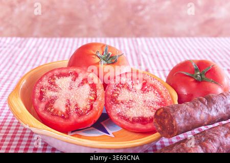 Un pomodoro tagliato a metà e condito con sale e pepe, servito accanto a un chorizo spagnolo piccante. Foto Stock