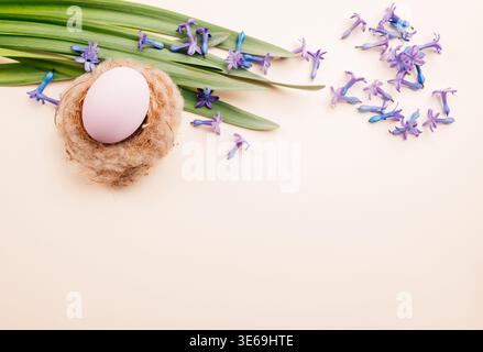 Sistemazione accogliente con delicato uovo rosa in piccolo nido con fiori e texture naturali Foto Stock
