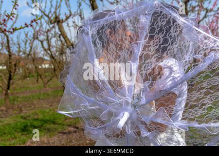 Coppia di nozze che si baciano dietro l'ombrello in pizzo nel frutteto Foto Stock