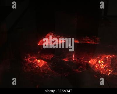 Riflessi rossi accesi nel cuore scuro, calore irradiato dai registri arcuati, scintille arancioni morbide, contorno piastrellato, Foto Stock
