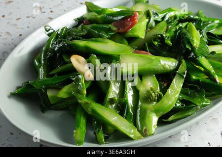 Vista ravvicinata di un piatto di gai lan fritti in padella e salsiccia. Foto Stock