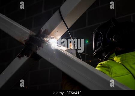 Saldatrice protettiva per casco che fonde il giunto del telaio in metallo su un supporto strutturale in acciaio, evidenziando la fabbricazione industriale e la manodopera qualificata nel settore edile Foto Stock