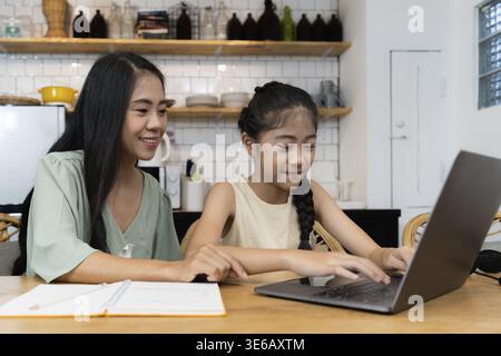 Concetto di scuola familiare e domestica. Madre asiatica insegna a sua figlia usando l'applicazione sul portatile a casa Foto Stock