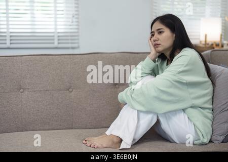 Una giovane donna con un abbigliamento casual siede su un divano, appare malata e premurosa, in un accogliente salotto Foto Stock