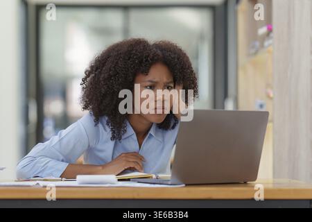 Ritratti una giovane donna d'affari afro-americana che guarda un notebook. Stress durante la lettura di notizie, report o e-mail. Problema online, finan Foto Stock