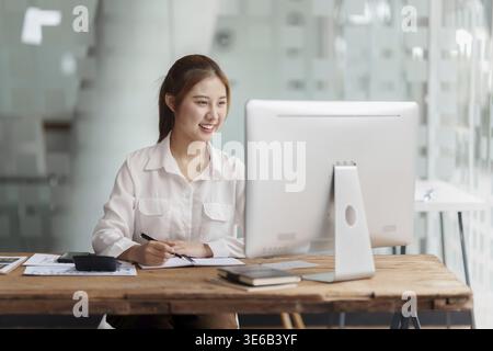 Bella giovane donna asiatica che usa un pc desktop in ufficio Foto Stock
