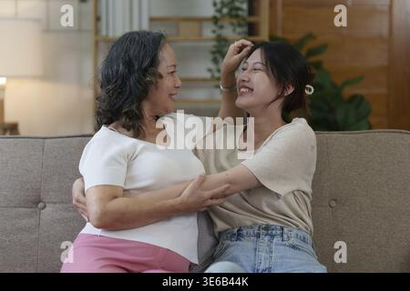 La donna asiatica anziana felice e la sua figlia adulta stanno coccolando sul divano Foto Stock
