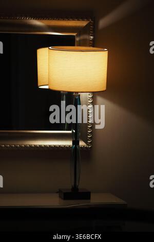 La lampada brilla accanto allo specchio in una stanza poco illuminata Foto Stock