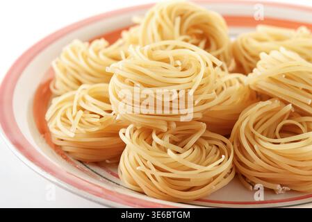 Primo piano di tagliolini crudi nidificano sul piatto Foto Stock