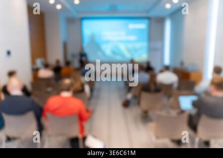 Immagine sfocata di un relatore aziendale che si presenta a un pubblico a una conferenza o a un seminario con uno schermo di proiezione che mostra diapositive. Foto Stock