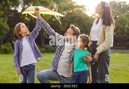 Famiglia felice che trascorre le vacanze estive insieme all'aperto nel parco, interagendo con gli aquiloni colorati Foto Stock