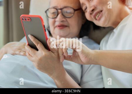 Senior multirazziale e giovane donna che ha videochiamata su uno smartphone a casa. Anziani e tecnologia. Messa a fuoco selettiva. Foto Stock