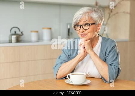 Buon giorno. Comfort rilassato anziano anziano anziano anziano donna nonna che beve bevande calde tè e caffè in cucina a casa. Donna matura che riposa goditi la calma mattinata nella casa moderna da sola. Concetto di pensione Foto Stock