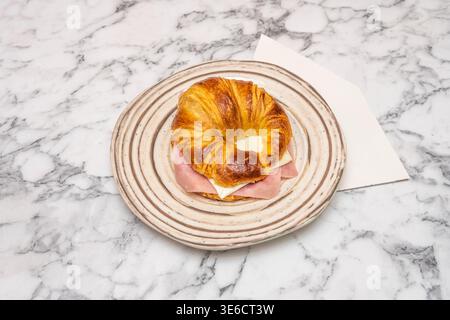 Una foto mattutina di un croissant ancora caldo dal forno, collocato su un tovagliolo di lino accanto alla marmellata fatta in casa e a un coltello al burro Foto Stock