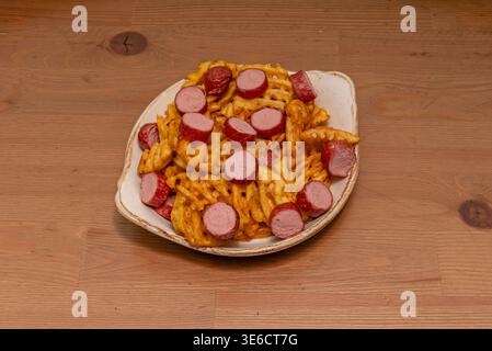 Salchipapas speciali con salsicce di ​​hot e patatine fritte spesse, condite con formaggio grattugiato fuso, Foto Stock
