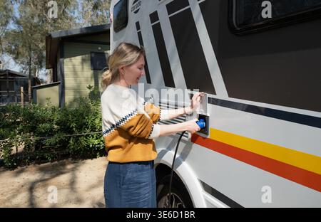 Donna che collega il cavo di alimentazione al camper in campeggio con allacciamento elettrico per viaggiare Foto Stock
