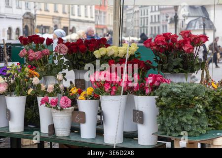 Vivace mercato dei fiori all'aperto con vivaci mazzi di rose rosse, rosa, gialle e verdi foglie, disposti in vasi bianchi a prezzi chiari Foto Stock