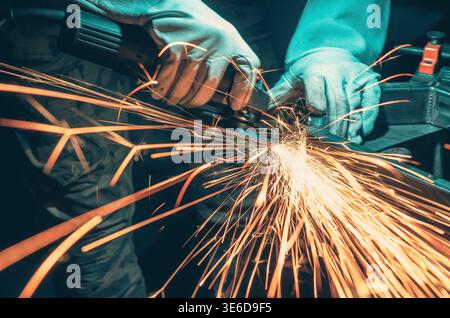 Scintille dorate derivanti dalla lucidatura dei metalli in officina. L'illuminazione intensa e lo sfondo scuro sfocato enfatizzano l'energia, il movimento e l'atmosfera industriale. Foto Stock