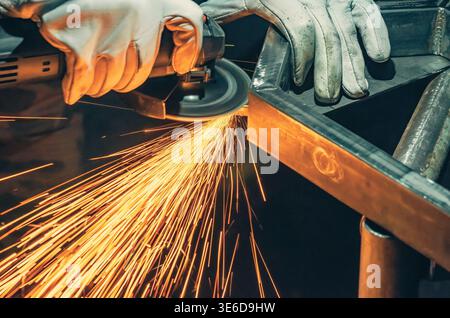 Scintille dorate derivanti dalla lucidatura dei metalli in officina. L'illuminazione intensa e lo sfondo scuro sfocato enfatizzano l'energia, il movimento e l'atmosfera industriale. Foto Stock