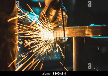 Scintille dorate derivanti dalla lucidatura dei metalli in officina. L'illuminazione intensa e lo sfondo scuro sfocato enfatizzano l'energia, il movimento e l'atmosfera industriale. Foto Stock