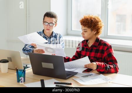 Brainstorming del lavoro di squadra. Diversi colleghi che lavorano insieme discutono di statistiche finanziarie. Gruppo di giovani felici e moderni seduti in un ufficio creativo a discutere di affari. Giovane squadra professionale Foto Stock