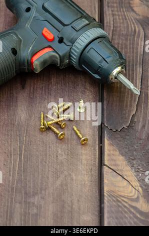 Trapano a batteria e viti su una superficie in legno da vicino. Foto Stock