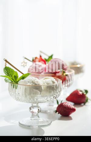 Composizione elegante con tre ciotole da dessert in vetro con bordi dorati, ripiene di palline di gelato alla vaniglia e fragole. Foto Stock