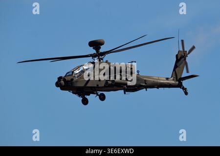 Un elicottero militare Apache verde scuro, con i suoi rotori che girano, viene catturato a metà volo contro un cielo blu luminoso e senza nuvole. Foto Stock