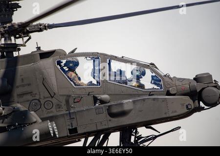 Due piloti in caschi da volo e uniformi mimetiche sono visibili all'interno dell'abitacolo tandem di un elicottero militare grigio scuro. Foto Stock