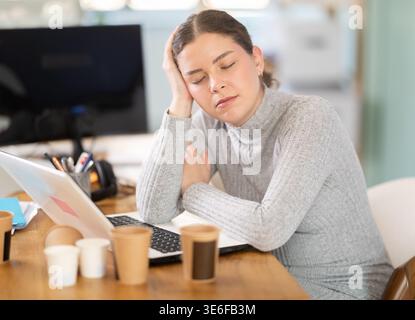 Giovane donna stanca che lavora con un notebook Foto Stock