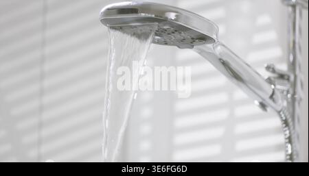 L'acqua fluisce da una doccia in un bagno durante il giorno, con la luce che splende attraverso le tende sulla parete Foto Stock